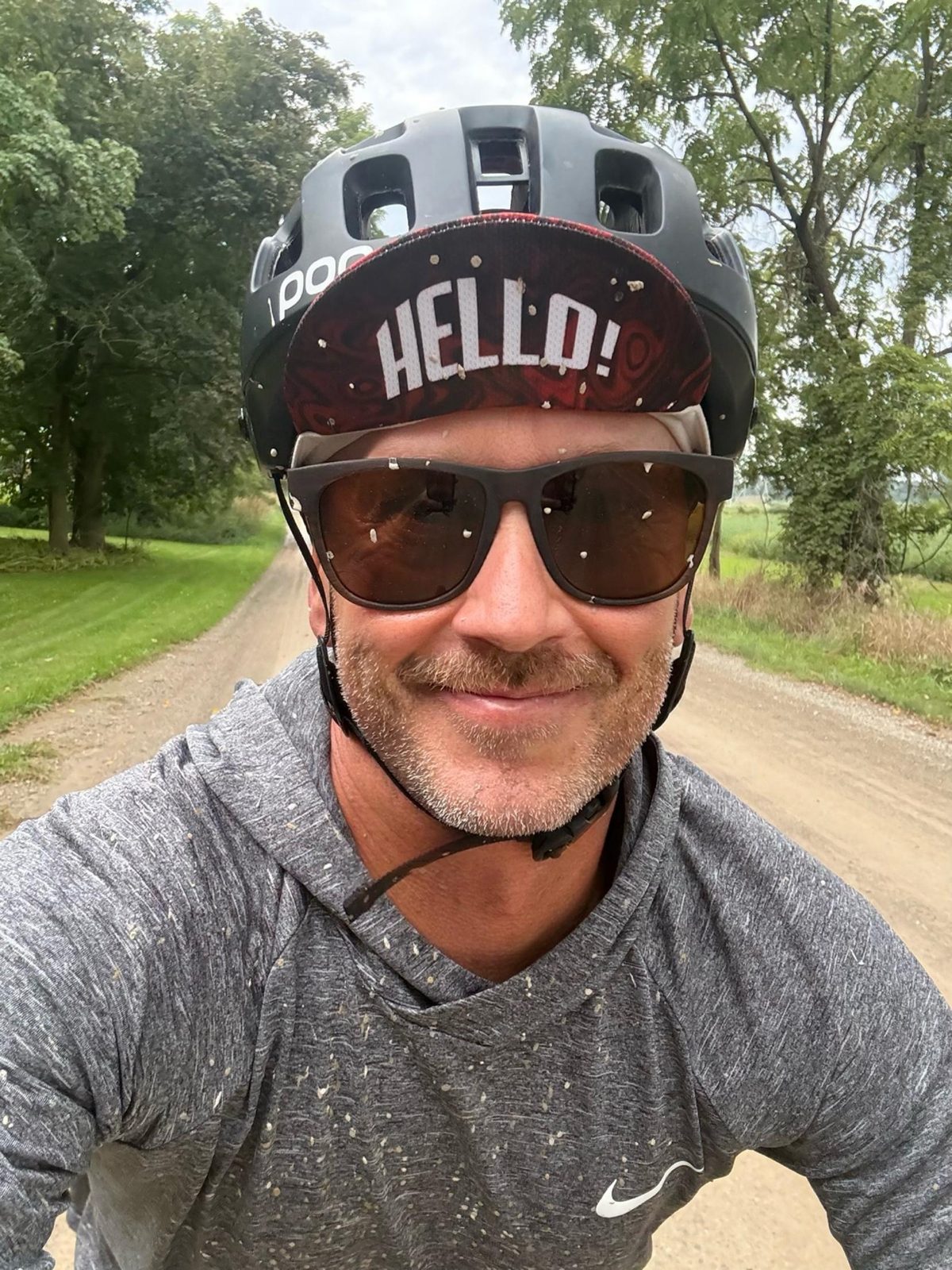 Kristian smiling in a cycling helmet and HELLO! cap on a gravel road